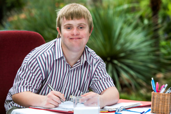 Close up portrait of young male student with down syndrome at study desk outdoors.